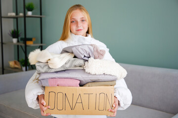 A child holds a donation box with clothes in the living room.