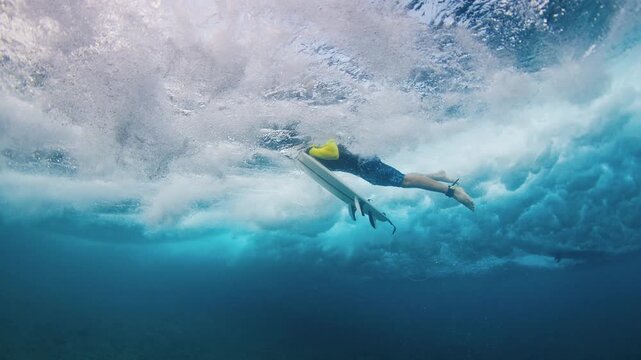 Surfer under the wave. Underwater view of the adult male surfer diving under the wave with surf board