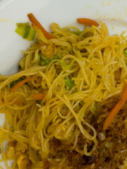 Chinese stir-fried rice noodles with chicken, vegetables and crispy topping served on a white plate.
