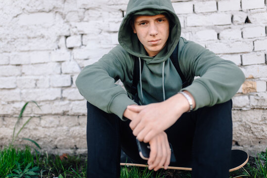 Young man in hoodie sitting on skateboard - Powered by Adobe