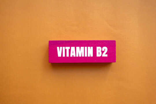 Vitamin B2 message written on pink wooden block on orange background. Conceptual Vitamin B2 symbol. Copy space.