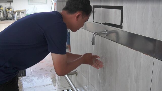 A Muslim man performs ablution at the mosque, gently washing his hands and face