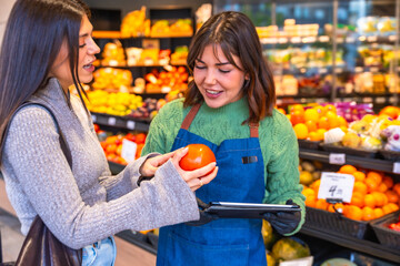 Employee assisting customer choosing fresh organic tomato