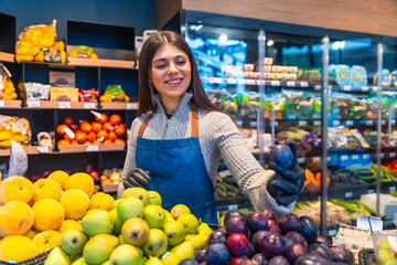 Young woman greengrocer preparing fresh plums in grocery store