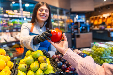 Greengrocer passing fresh tomato to customer in supermarket