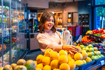 Woman buying fresh fruit using reusable bag in supermarket