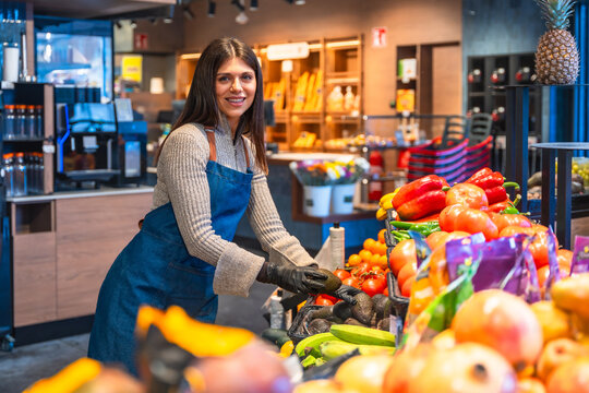 Woman employee arranging fresh produce in grocery store