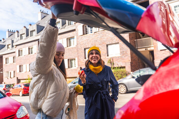 Happy girlfriends standing near car trunk, smiling and eating apples