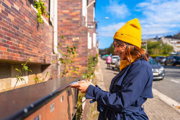 Woman sending letter through mailbox on urban street