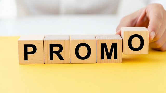 A hand placing a wooden block with the letter o to complete the word promo on a yellow surface
