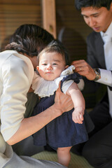 A woman is holding a baby in a blue dress. The baby is wearing a white collar