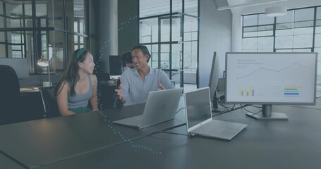 Talking pair wearing sleeveless top and blue shirt at table in office with silver laptops, monitor © vectorfusionart