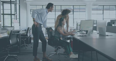 Collaborating team leaning around desk in open office, woman in tank top viewing monitor charts