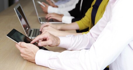 Tapping man wearing pink button shirt holding black tablet at office table with laptops, copy space