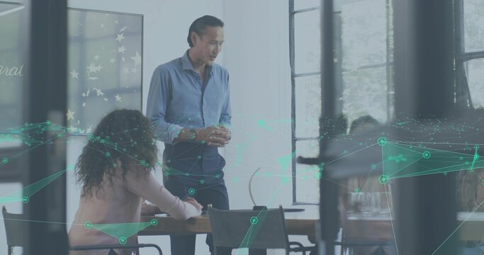 Presenting Asian male in light shirt addressing team at office table with glass frames teal overlay