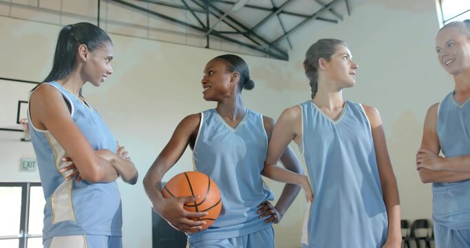 Talking four female players wearing light blue jerseys standing midcourt, holding orange basketball - Powered by Adobe