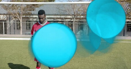 Standing male soccer player wearing red kit on green turf, facing regulation goal, cyan circles