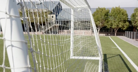 Showing white metal goalpost and knotted net on artificial turf field, with sideline and building