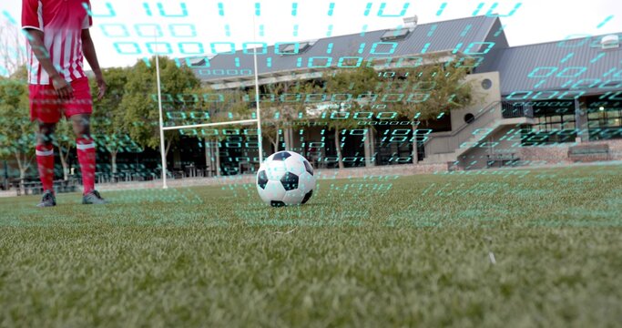 Resting soccer ball centered on turf, player wearing red-striped kit, goalposts and binary overlay - Powered by Adobe
