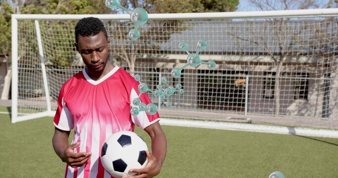 Standing player in red-and-white kit holding soccer ball on yard pitch, with goal and teal bubbles