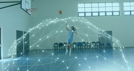 Leaping mid-adult woman wearing light uniform releasing basketball toward hoop at gym, digital mesh