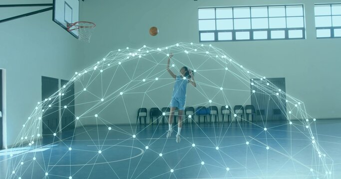 Leaping mid-adult woman wearing light uniform releasing basketball toward hoop at gym, digital mesh - Powered by Adobe