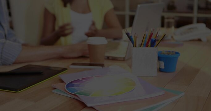 Showing color wheel resting on folders at wooden table, pencil cup and woman in yellow cardigan