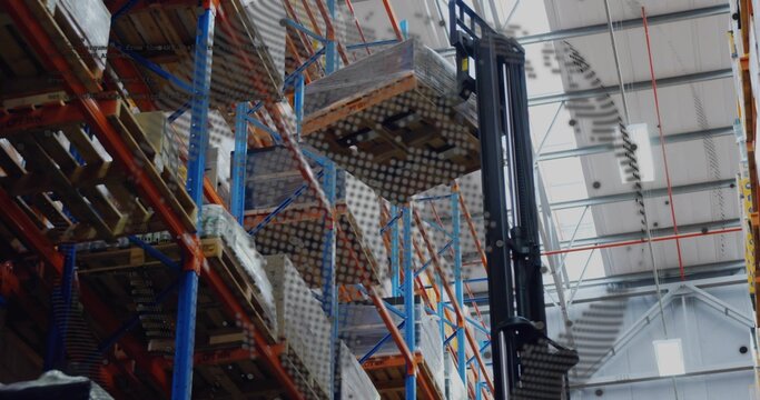 Lifting forklift mast holding wrapped pallet in large warehouse, showing pallet racking