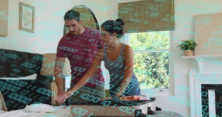 Packing couple leaning over bed at home, arranging clothes in open carry-on suitcase