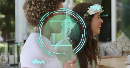 Chatting women wearing floral headband and white top sitting at patio table with teacup HUD overlay