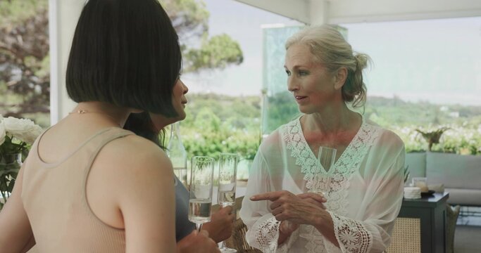 Speaking senior woman wearing lace blouse gesturing on right patio, with champagne flutes, flowers - Powered by Adobe