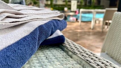 Neatly stacked blue and white stripes towels sit beside the water, inviting relaxation during a warm morning by a hotel swimming pool. Relaxing luxury resort atmosphere, summer vacation, leisure, hosp