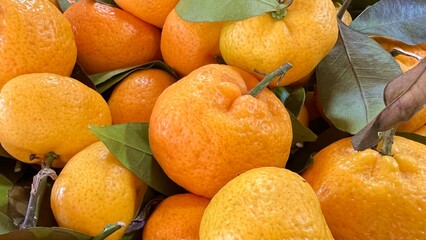Pile of fresh mandarins with glossy orange skin and green leaves on traditional market, perfect for themes of organic produce, healthy eating, farmers market, and natural food backgrounds.