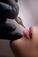 Fashion photo of lip tattoo procedure on female lips with tattoo machine