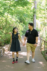 Obraz premium A man and woman are walking on a path in a forest. The man is wearing a black shirt and khaki shorts, while the woman is wearing a black dress. They are holding hands