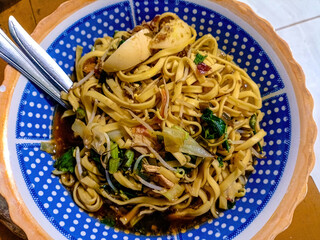 Mie celor is an indonesian noodle dish served in a coconut milk and shrimp based broth, specialty from palembang. Served on a blue plate with polka dots and a pair of spoons, close up shot.