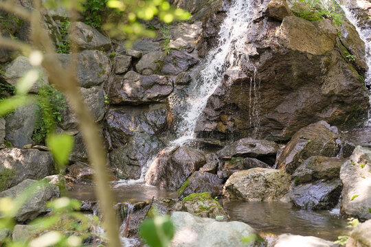 A small waterfall is flowing down a rocky hillside. The water is crystal clear and the rocks are jagged and rough. The scene is peaceful and serene