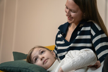Two sisters lying together on a cozy yellow sofa at home, older sister gently caressing younger sister hair, symbolizing care, love, and family bonding