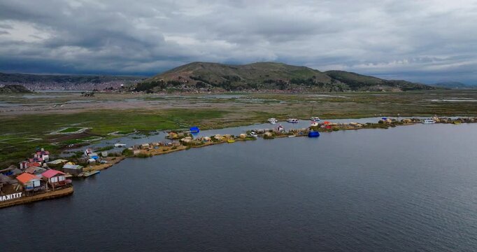 Aerial drone view of the Uros floating islands on Lake Titicaca near Puno, Peru. The man-made reed islands are dotted with traditional houses and boats, with mountains in the background