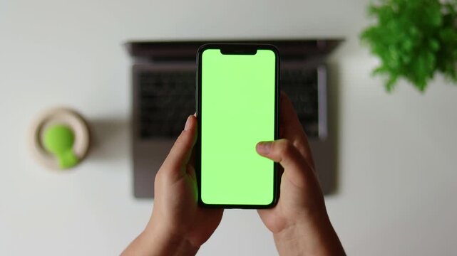 Woman sit use digital tech cell phone, green screen mock up. Hand scroll iphone web site, swipe like photos. Girl hold mobile closeup. Chroma key page. Cozy office background. Online app copy space.
