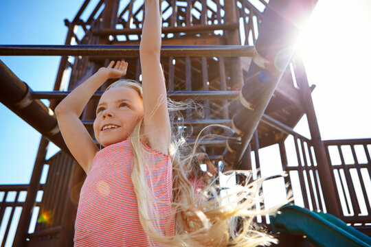 Kid, girl and monkey bars at playground for adventure, fun or explore on weekend holiday. Child, smile or hang outdoor at park, climbing or play with energy on vacation for development with low angle