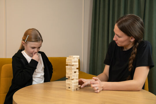 Mother and daughter enjoying a game of jenga, with the mother carefully removing a block and the daughter watching with anticipation during family leisure time