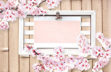 Spring background with a branch of blooming sakura and retro wooden frame with blank paper sheet on bamboo wall. Sakura blossoming season in Japan. Vintage style mood board layout. Copy space for text