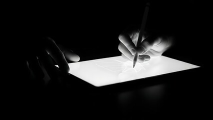 Close-up of hands drawing digital art on a glowing tablet in a dark room.