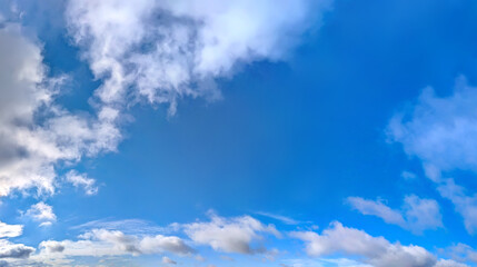 Fototapeta premium Cloudscape white clouds panorama. A wide panoramic of low-flying cumulus cloud of varying sizes. Voluminous space-occupying lesions of steam against a blue background. The sky in serene slow motion.