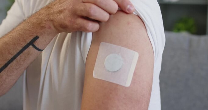 Man shows patch sensor for diabetes glucose. Wearable device on upper arm tracks levels, supporting health management and doctor-guided monitoring at home. Idea: home glucose monitor wearable.