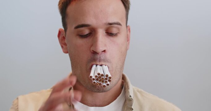 Man smoking cigarettes, smoke shows health harm. Close portrait shows a mouthful of cigarettes, a blunt metaphor for addiction, nicotine dependence, habit. Severe health danger from smoking.