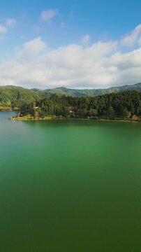 Aerial vertical footage capturing the historic Nossa Senhora das Vit&oacute;rias Chapel on Furnas Lake, S&atilde;o Miguel, Azores. This iconic neo-Gothic landmark is surrounded by lush natural park scener
