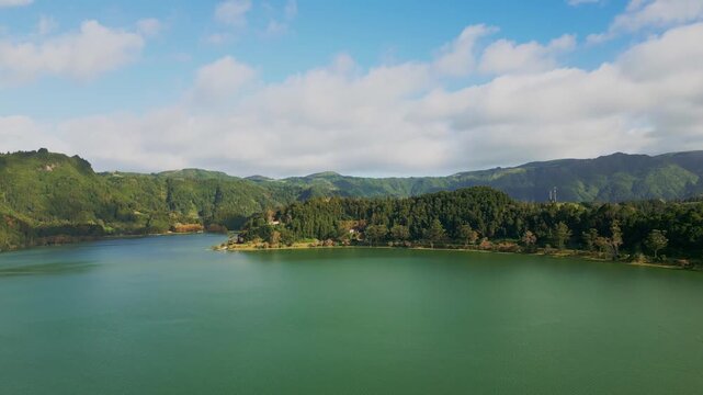 Aerial horizontal footage capturing the historic Nossa Senhora das Vit&oacute;rias Chapel on  Furnas Lake, S&atilde;o Miguel, Azores. This iconic neo-Gothic landmark is surrounded by lush natural park scener