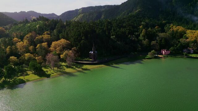 Aerial horizontal footage capturing the historic Nossa Senhora das Vit&oacute;rias Chapel on  Furnas Lake, S&atilde;o Miguel, Azores. This iconic neo-Gothic landmark is surrounded by lush natural park scener